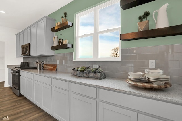 kitchen with appliances with stainless steel finishes, white cabinetry, light stone counters, dark hardwood / wood-style flooring, and decorative backsplash