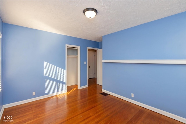 unfurnished bedroom with a textured ceiling, a closet, and dark hardwood / wood-style floors