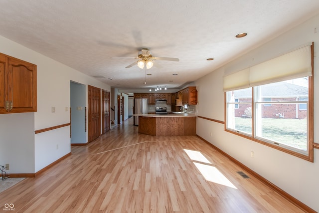 kitchen featuring brown cabinetry, baseboards, light wood finished floors, a peninsula, and a textured ceiling