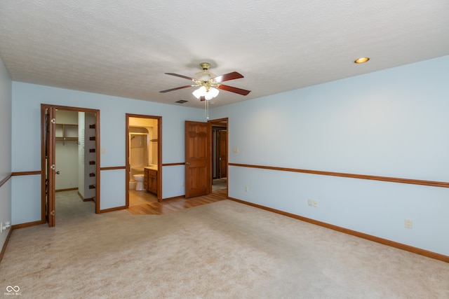 unfurnished bedroom featuring a walk in closet, light carpet, baseboards, and a closet