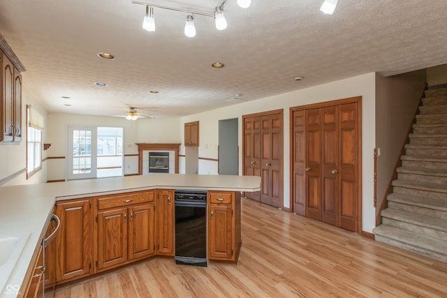 kitchen with light wood-style flooring, a textured ceiling, a peninsula, a fireplace, and light countertops