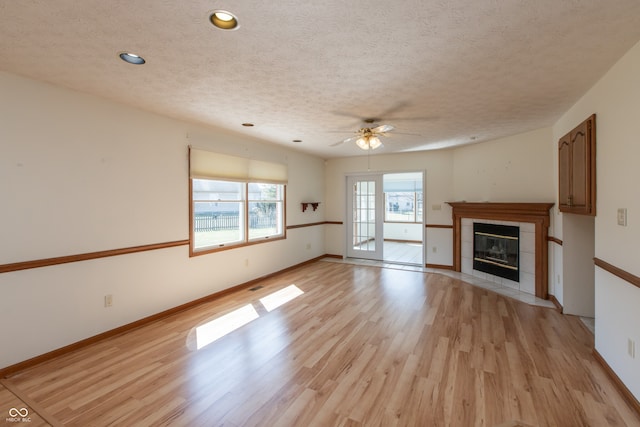 unfurnished living room with light wood-style flooring, a tile fireplace, a textured ceiling, and baseboards