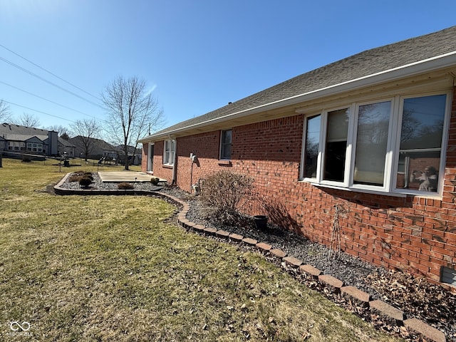 view of side of home with brick siding, a lawn, and a shingled roof