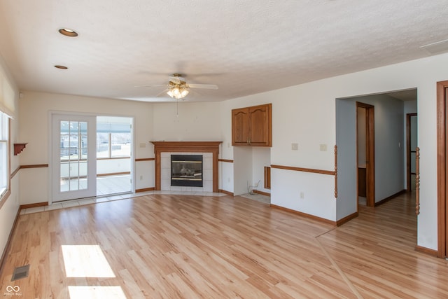 unfurnished living room featuring baseboards, visible vents, light wood-style flooring, a textured ceiling, and a tiled fireplace