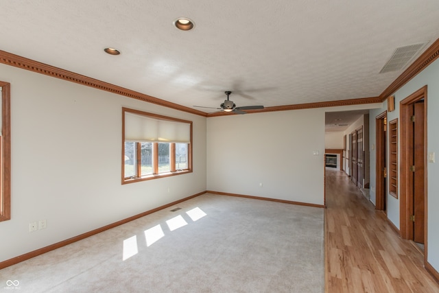 empty room with a ceiling fan, baseboards, visible vents, light wood finished floors, and crown molding