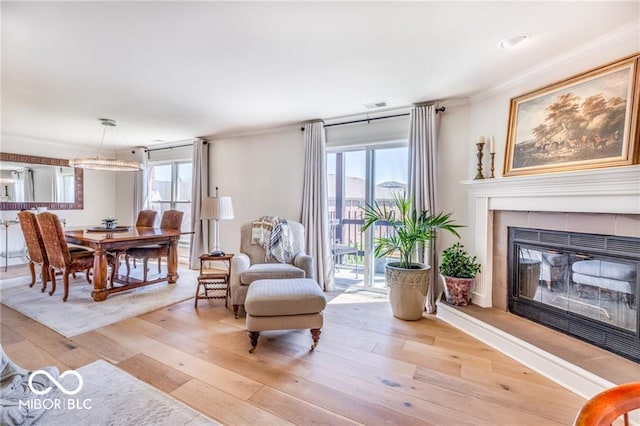 living area featuring a tiled fireplace, crown molding, and light hardwood / wood-style flooring