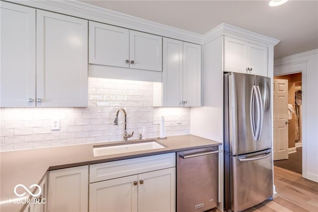 kitchen featuring sink, white cabinetry, light wood-type flooring, stainless steel appliances, and backsplash