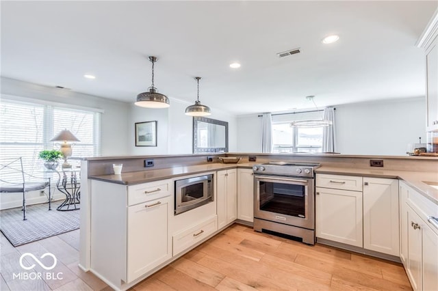 kitchen featuring appliances with stainless steel finishes, decorative light fixtures, light wood-type flooring, and white cabinets