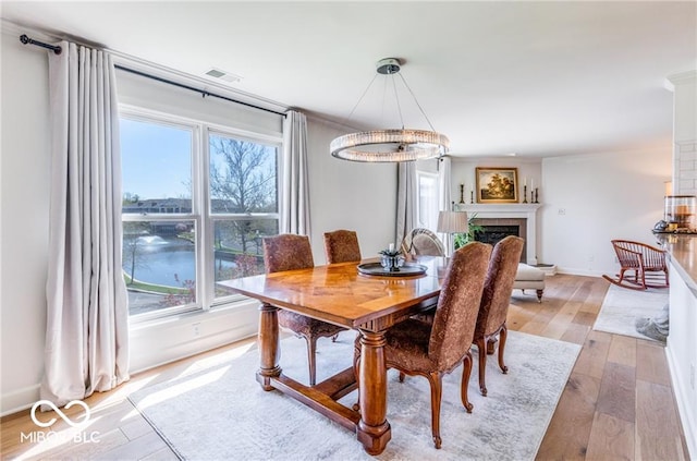 dining area featuring a tiled fireplace, light hardwood / wood-style floors, and a water view