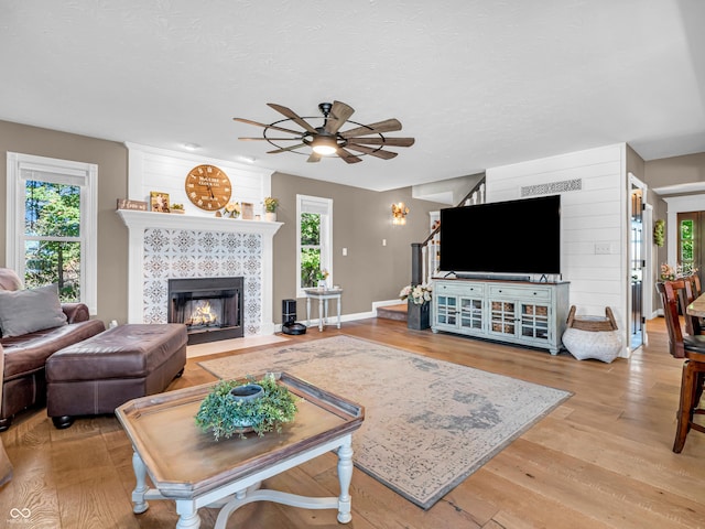 living room with ceiling fan, light wood-type flooring, a fireplace, and a textured ceiling