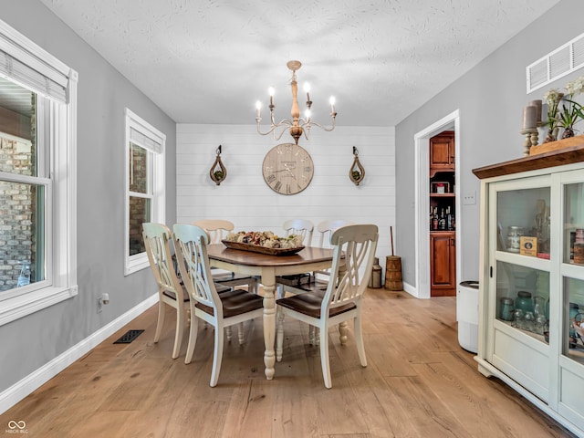 dining room with a textured ceiling, a chandelier, light hardwood / wood-style floors, and wooden walls