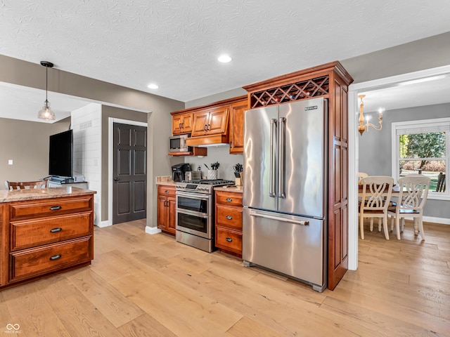 kitchen with hanging light fixtures, appliances with stainless steel finishes, light stone counters, and light hardwood / wood-style floors