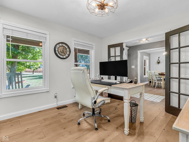 office with light wood-type flooring, an inviting chandelier, and a wealth of natural light