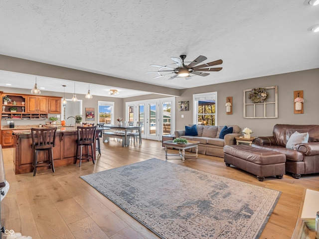 living room featuring ceiling fan, a textured ceiling, french doors, and light wood-type flooring