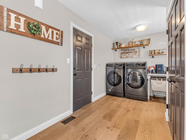 laundry room with light wood-type flooring, separate washer and dryer, and a textured ceiling