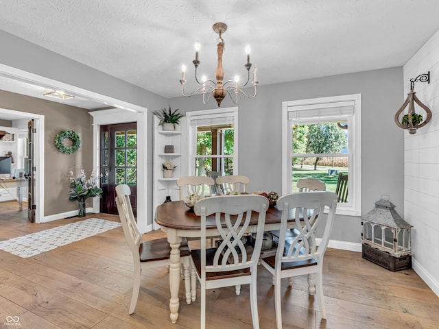 dining area with light hardwood / wood-style floors, a textured ceiling, and a notable chandelier