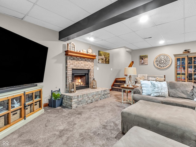 living room featuring a brick fireplace, carpet flooring, and a drop ceiling