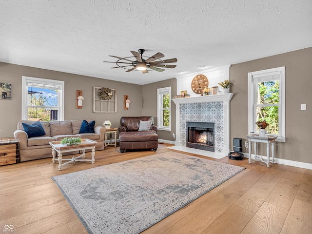 living room with a textured ceiling, ceiling fan, a fireplace, and light hardwood / wood-style flooring