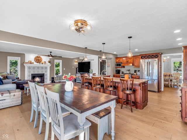 dining room with a textured ceiling, ceiling fan, light hardwood / wood-style flooring, and a tiled fireplace