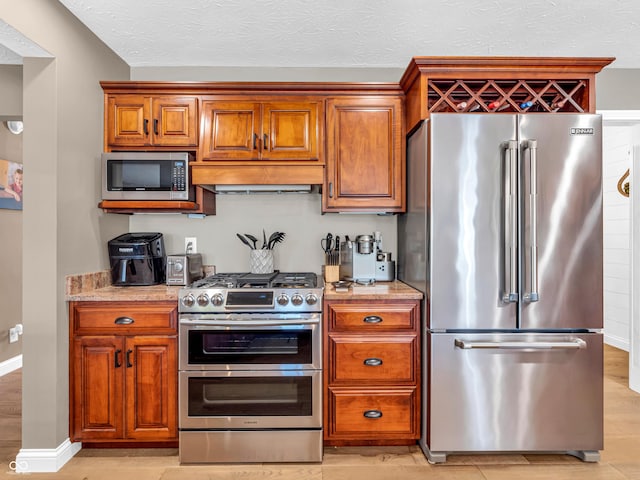 kitchen with light stone counters, premium range hood, stainless steel appliances, and light hardwood / wood-style flooring