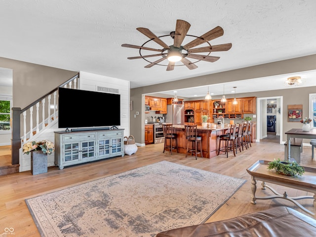 living room with ceiling fan, washer / clothes dryer, a textured ceiling, and light hardwood / wood-style floors