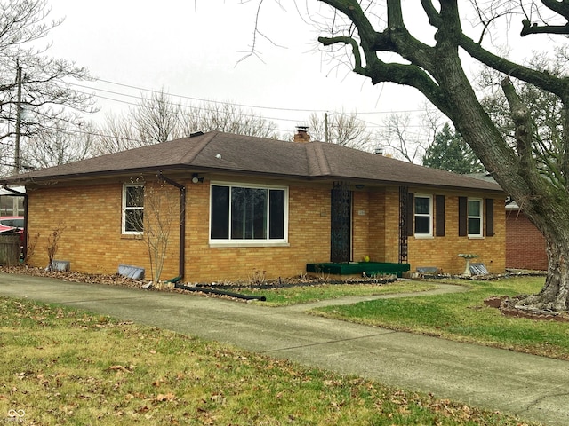 ranch-style home with brick siding, a chimney, a shingled roof, and a front lawn