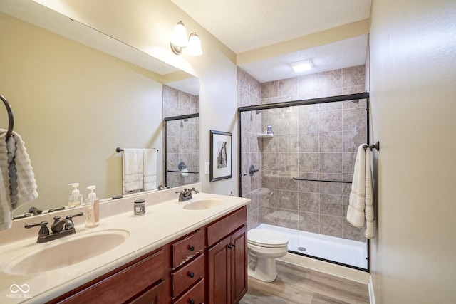 bathroom with hardwood / wood-style flooring, toilet, a shower with shower door, and vanity