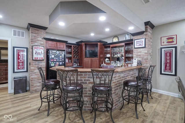 bar featuring light hardwood / wood-style flooring and black fridge