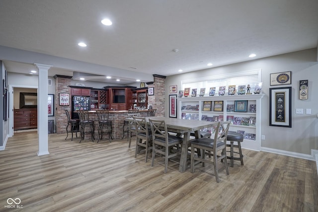 dining area with hardwood / wood-style floors, ornate columns, brick wall, and bar