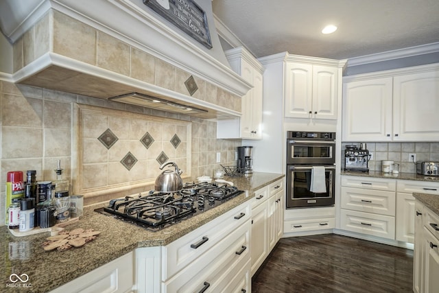 kitchen featuring backsplash, white cabinets, dark stone counters, gas cooktop, and multiple ovens