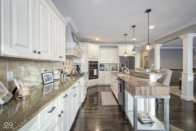 kitchen featuring decorative light fixtures, white cabinetry, stainless steel appliances, dark stone countertops, and decorative columns