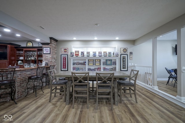 dining space with hardwood / wood-style flooring, a textured ceiling, and bar