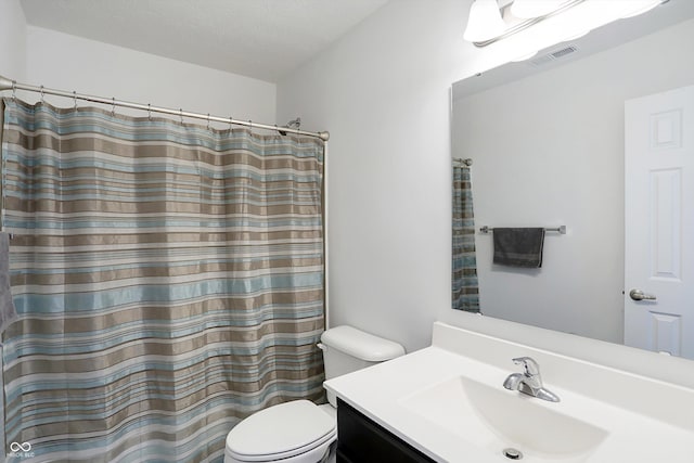 bathroom featuring a textured ceiling, toilet, vanity, and walk in shower