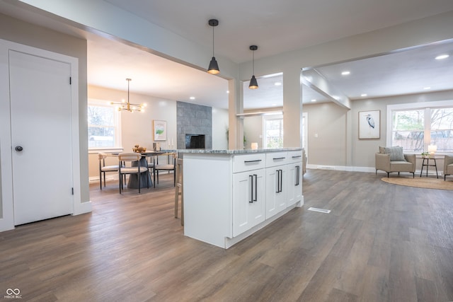 kitchen featuring light stone countertops, pendant lighting, a kitchen island, white cabinetry, and dark hardwood / wood-style flooring