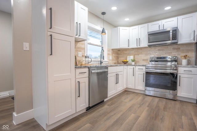 kitchen with pendant lighting, white cabinetry, stainless steel appliances, and hardwood / wood-style floors