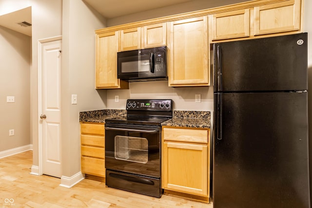 kitchen with dark stone countertops, light brown cabinetry, light hardwood / wood-style flooring, and black appliances