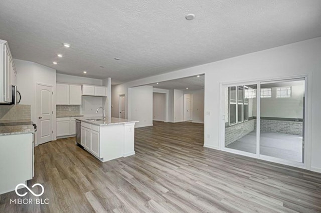 kitchen with white cabinetry, sink, decorative backsplash, and an island with sink