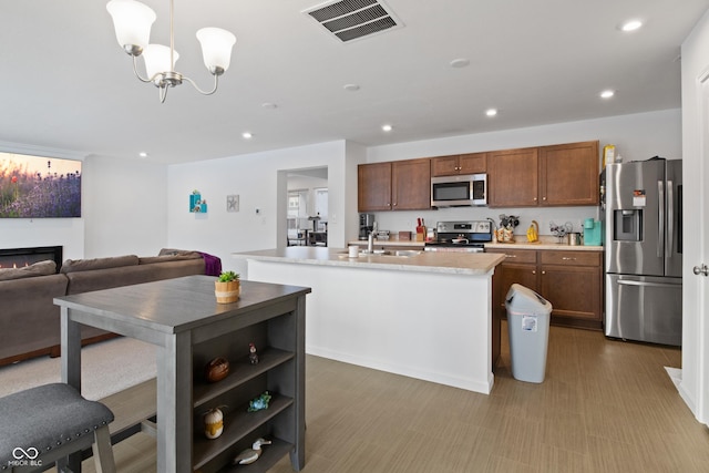 kitchen with sink, pendant lighting, stainless steel appliances, and a kitchen island with sink