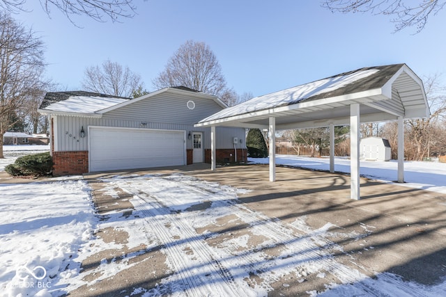 snow covered property with a garage, a storage shed, and a carport