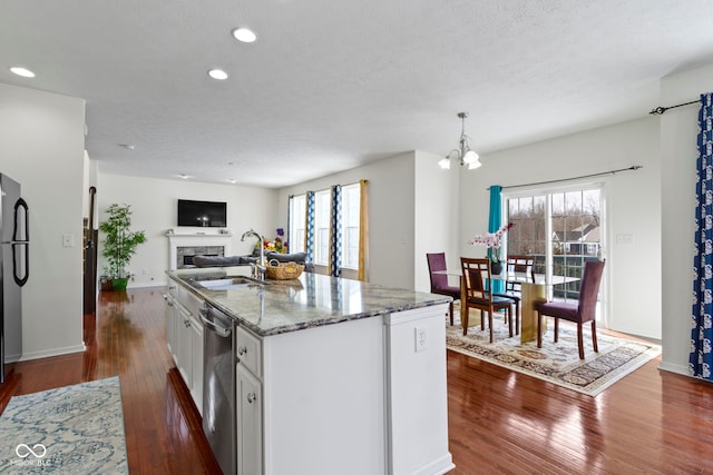 kitchen featuring white cabinets, dishwasher, light stone counters, a fireplace, and a sink