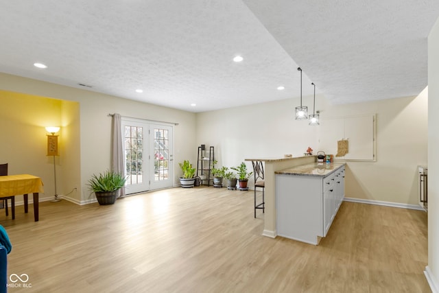 kitchen with a textured ceiling, light wood-style flooring, a peninsula, baseboards, and a kitchen bar