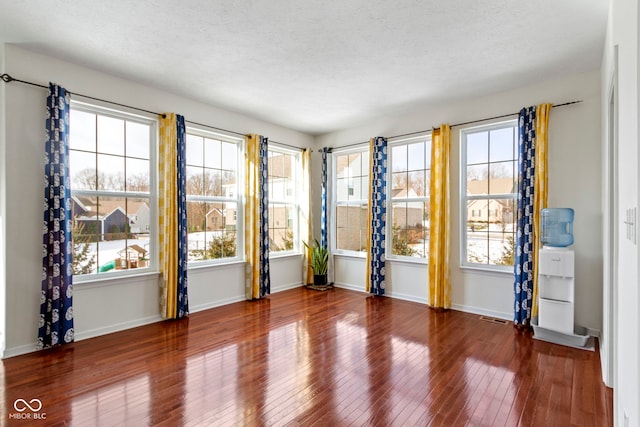 unfurnished room with a healthy amount of sunlight, visible vents, baseboards, and hardwood / wood-style flooring