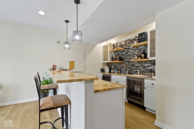 kitchen with a breakfast bar, wine cooler, light wood-type flooring, and backsplash