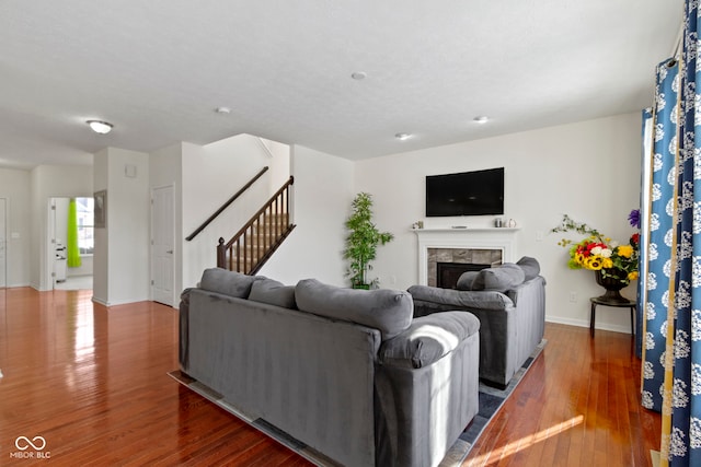 living area featuring stairs, baseboards, a tiled fireplace, and wood finished floors