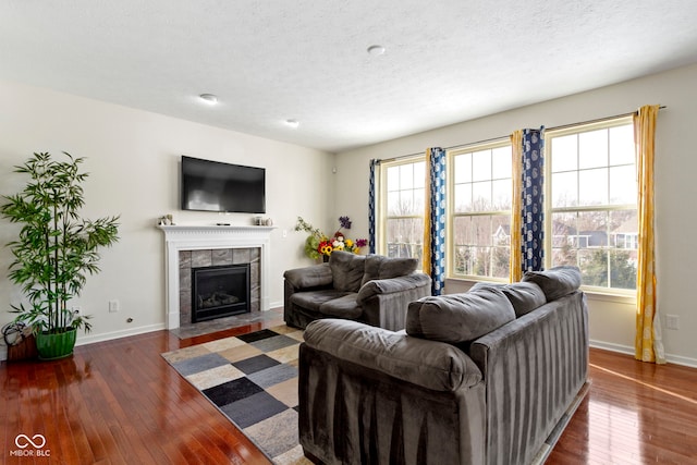 living room featuring a tile fireplace, wood-type flooring, a textured ceiling, and baseboards