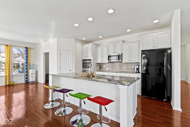 kitchen featuring a center island with sink, appliances with stainless steel finishes, dark wood-style flooring, and backsplash