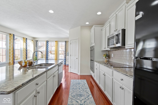 kitchen with an island with sink, dark wood-style floors, a sink, black appliances, and backsplash