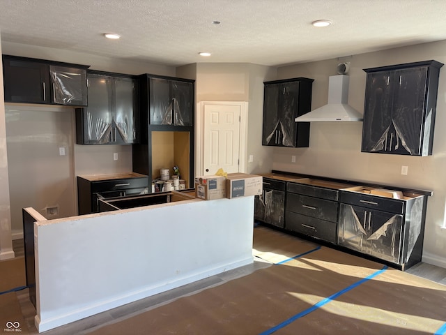 kitchen featuring a kitchen island, hardwood / wood-style floors, a textured ceiling, and wall chimney exhaust hood