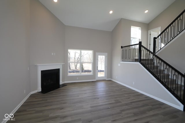 unfurnished living room with dark wood-type flooring, high vaulted ceiling, a fireplace, baseboards, and stairs