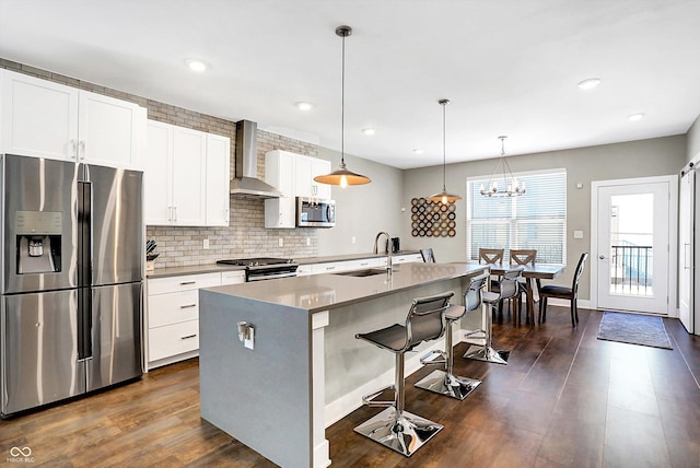 kitchen with hanging light fixtures, appliances with stainless steel finishes, wall chimney exhaust hood, and a kitchen island with sink